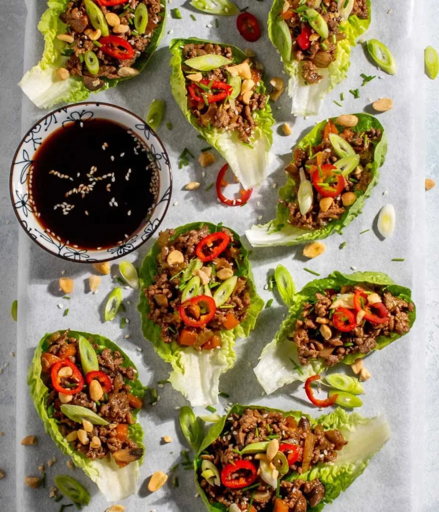 Yuk sung lettuce wraps assembled on a platter next to a bowl of stir-fry sauce.