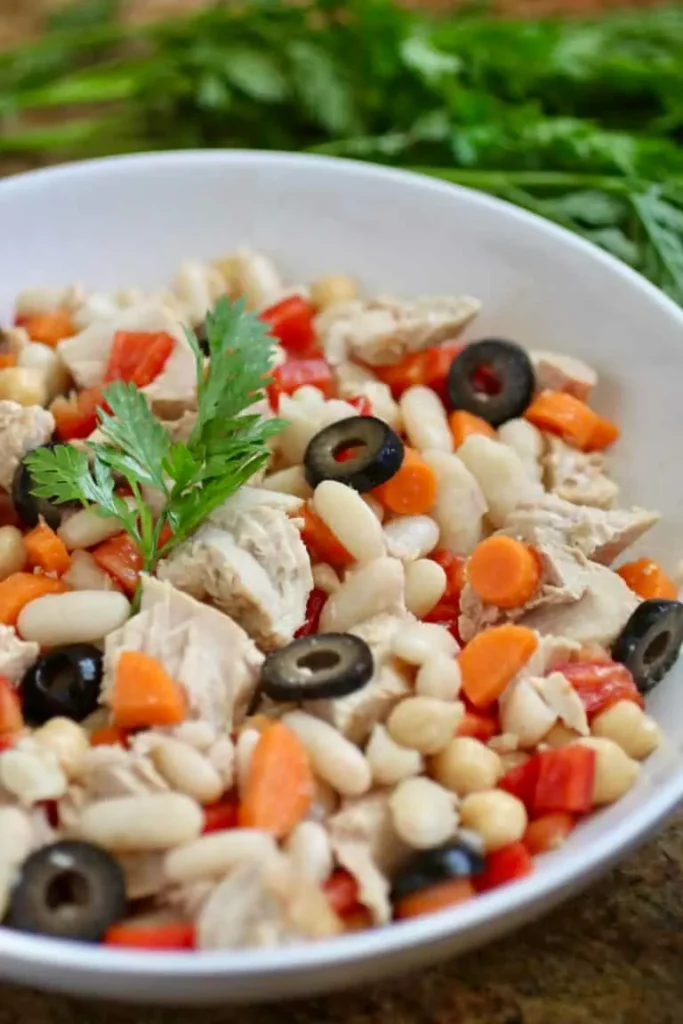 A close-up of cannellini beans and olives in a large bowl on a table.