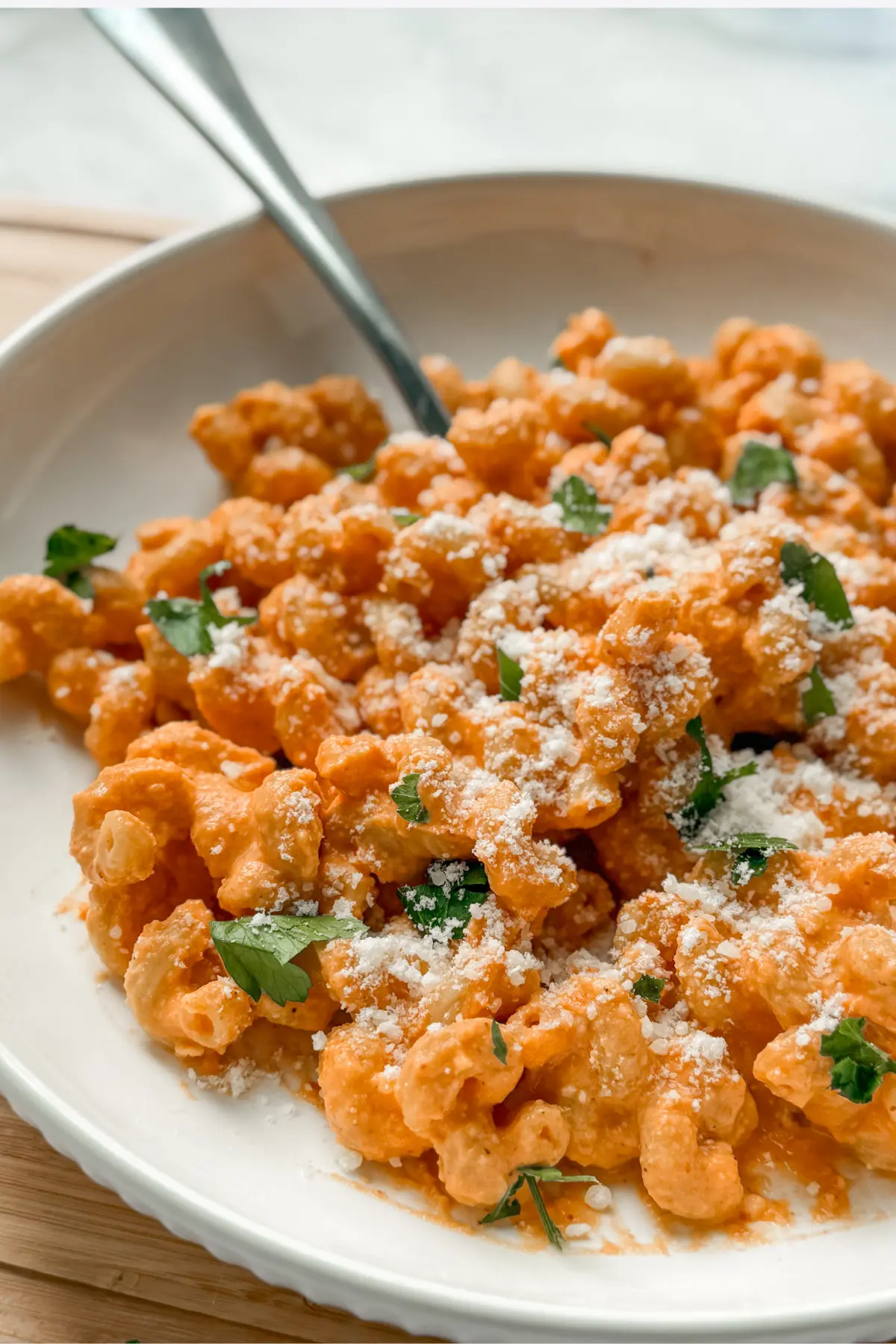 A close-up of a bowl of cottage cheese pasta with hidden sweet potatoes topped with parmesan cheese with a fork in it on a table.
