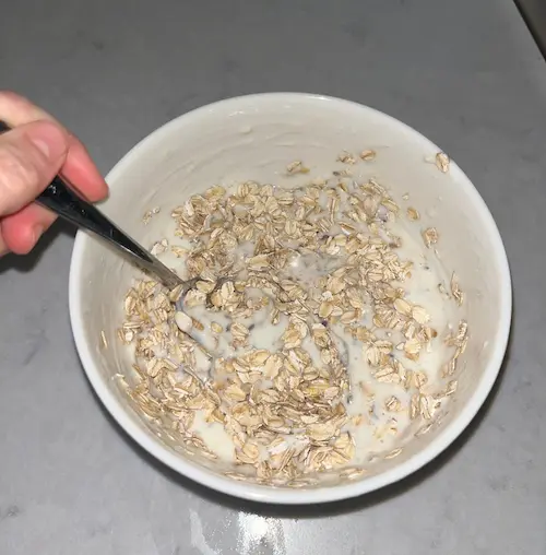 Combining the oats with the yogurt mixture in a white bowl.