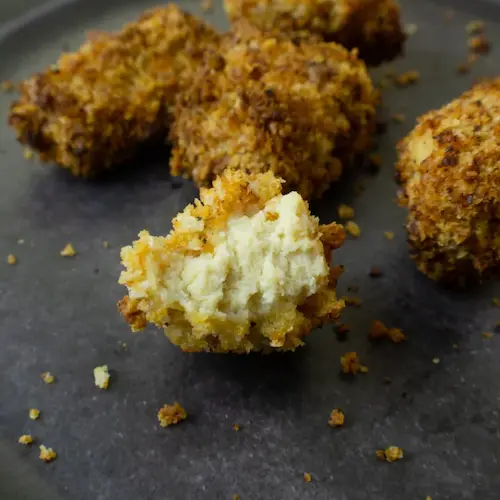A close-up of a half-bitten tofu nugget next to more tofu nuggets on a baking sheet.