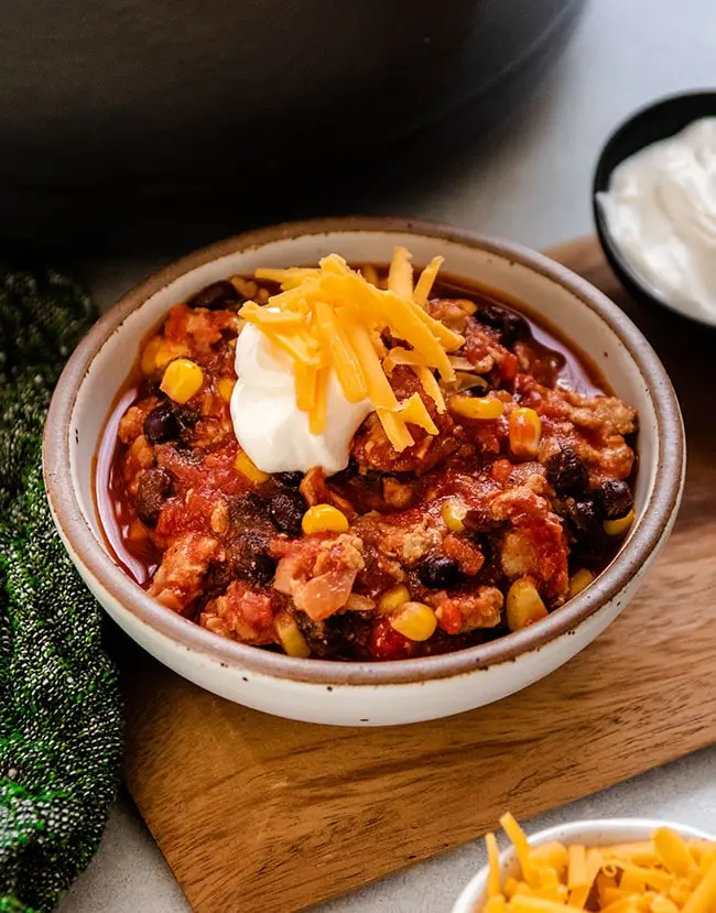 Turkey, black bean and corn chili topped with cheese in a small bowl on a table.