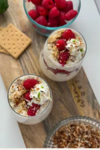 A birds-eye view of two overnight oats topped with raspberries and whipped on a table next to a bowl of raspberries.