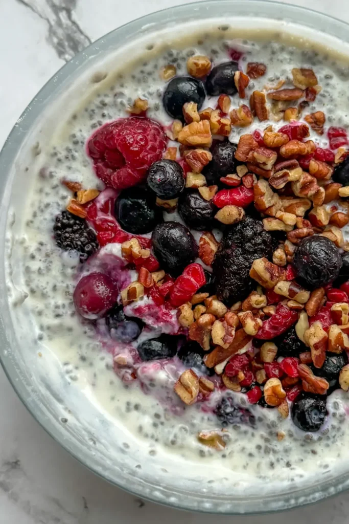 A close-up of a creamy chia breakfast bowl topped with pecans and mixed berries on a counter.