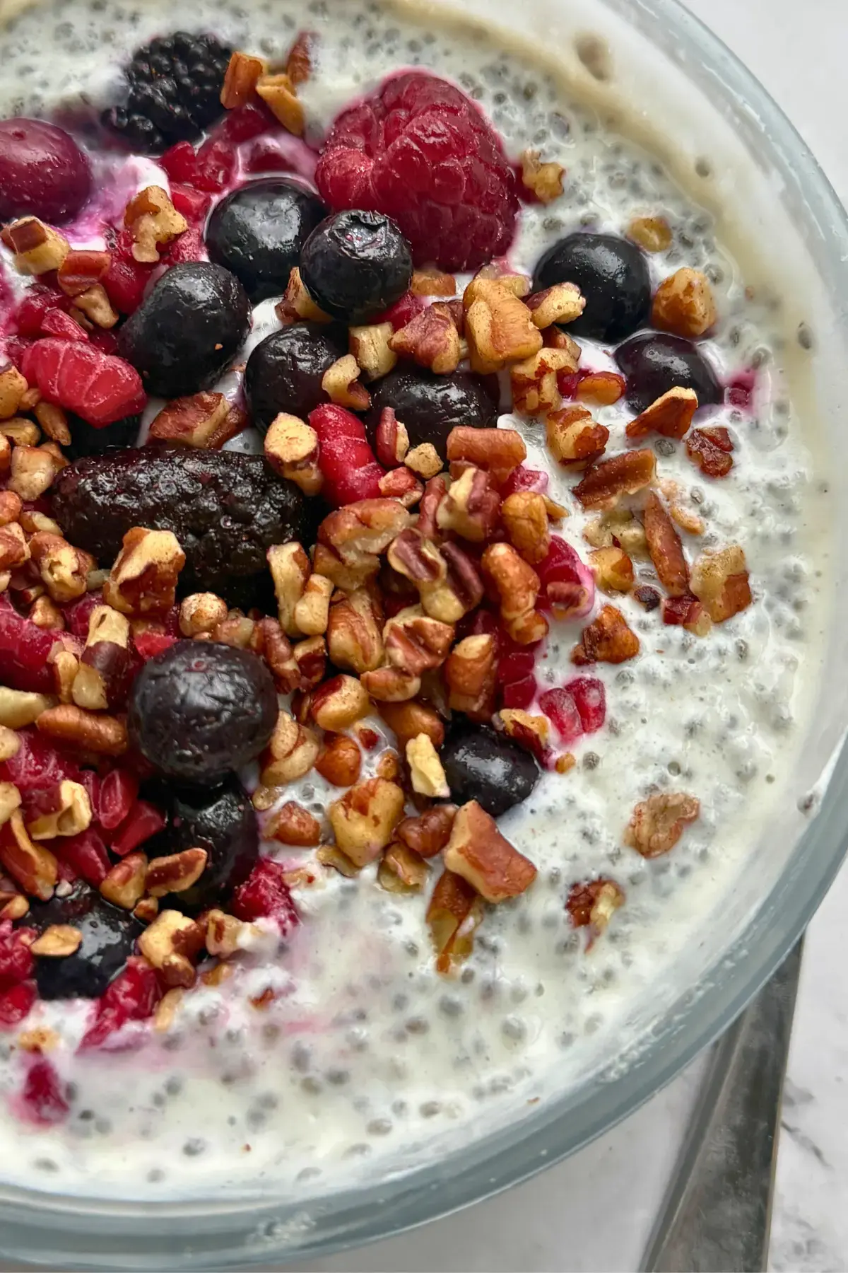 A chia breakfast bowl topped with chopped pecans, fruit and honey on a counter next to a spoon.