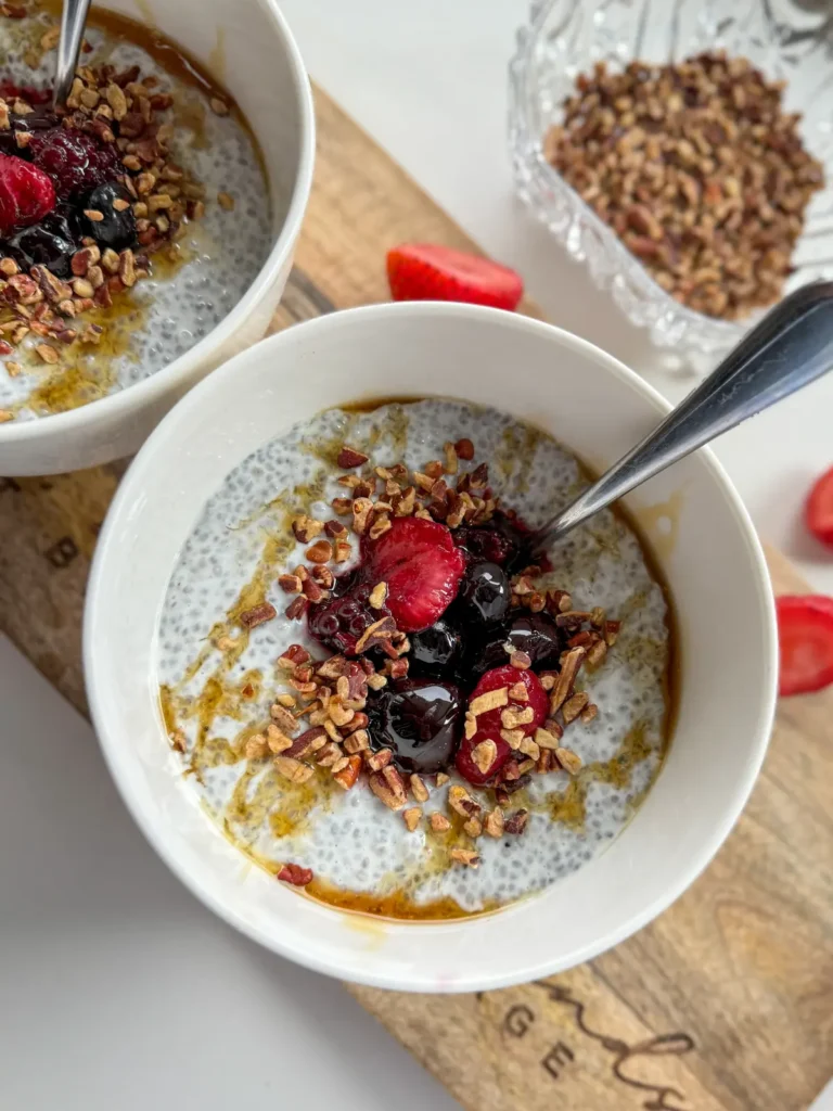 A high protein and fiber chia breakfast bowl topped with fruit, chopped pecans and honey on a wooden cutting board.