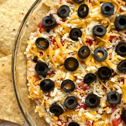 A birds-eye view of a high protein taco dip with cottage cheese in a glass baking dish surrounded by tortilla chips.