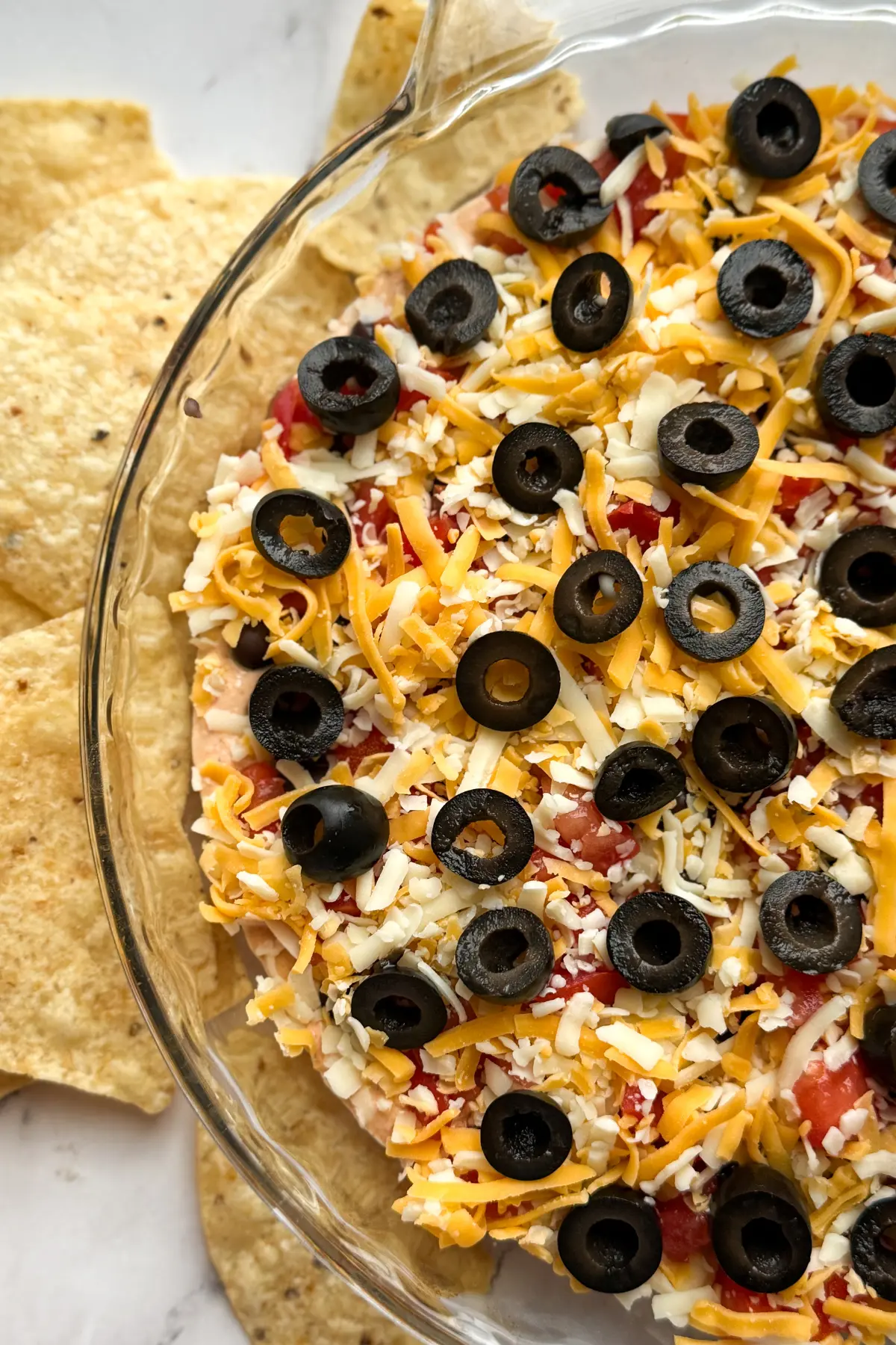 A birds-eye view of a high protein taco dip with cottage cheese in a glass baking dish surrounded by tortilla chips.