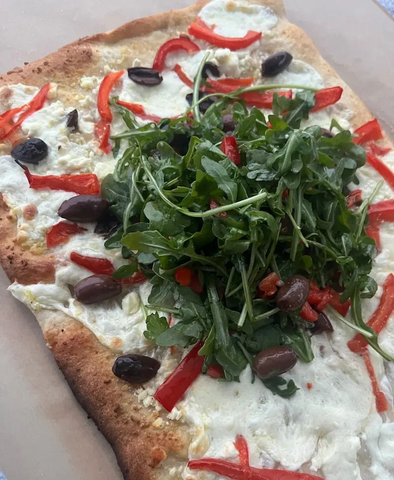 A close-up of Mediterranean Diet Pizza topped with arugula and olives on a parchment paper lined cutting board.