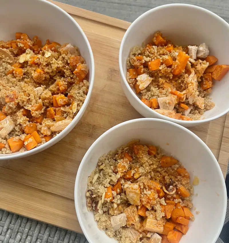 3 sweet potato quinoa bowls in white bowls on a cutting board.