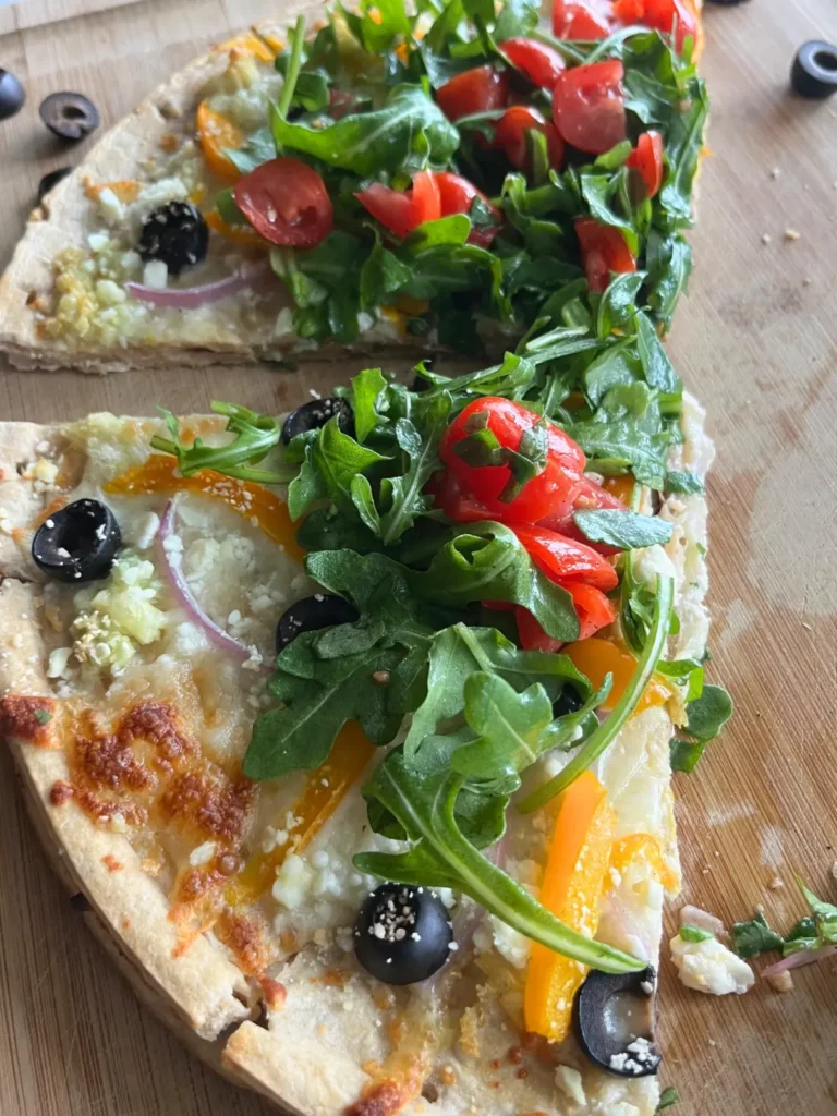 A close-up of two slices of Mediterranean diet pizza on a wooden cutting board after slicing.