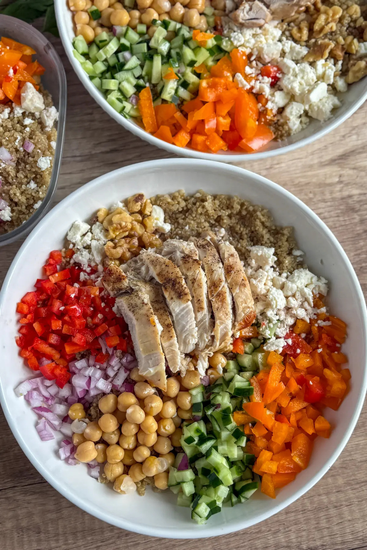 Two fully assembled Mediterranean grain bowls on a counter next to a meal prep container of a bowl.