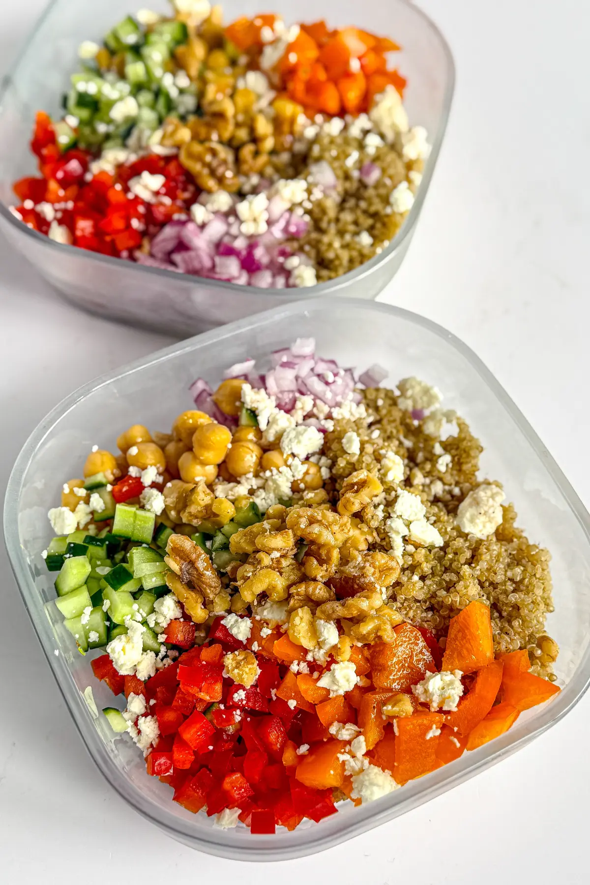Two Mediterranean grain bowls in glass meal prep storage containers.