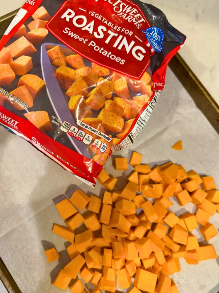 Diced sweet potatoes on a baking sheet lined with parchment paper next to a bag of frozen air fryer sweet potatoes.