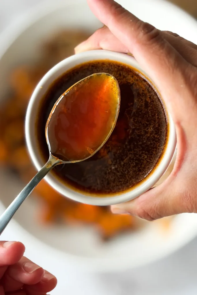 A bowl of the honey sriracha sauce with a spoonful above it.