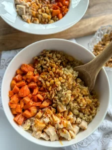A large bowl with roasted sweet potatoes, chopped walnuts, quinoa, and chicken drizzled with honey sriracha sauce on a counter.