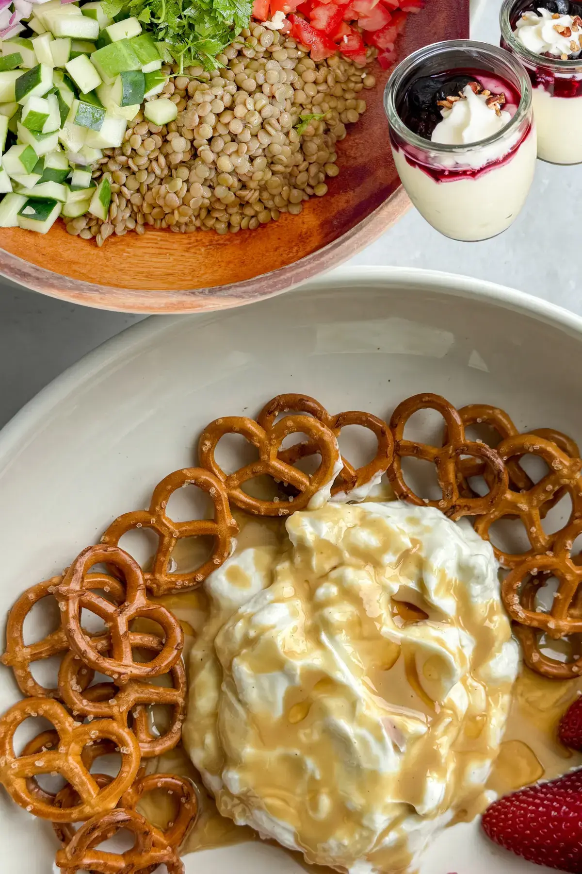 A Greek yogurt tahini plate next to protein pudding next to a lentil salad on a counter.