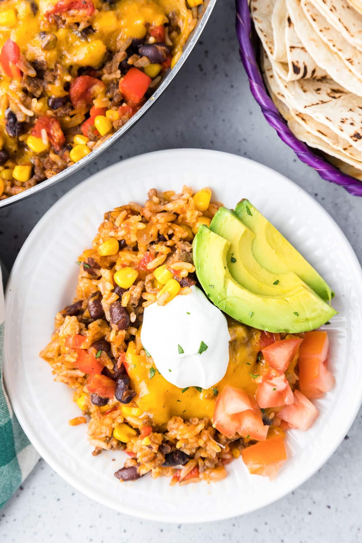A fork digging into a beef burrito bowl with a sliced avocado on the side.