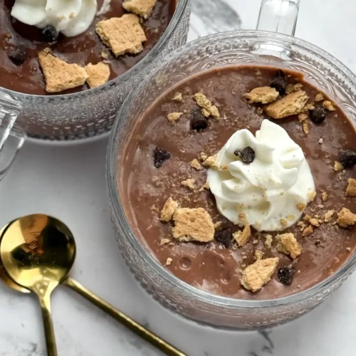 A birds-eye view of two dark chocolate puddings topped with whipped cream and graham crackers in bowls on a counter.