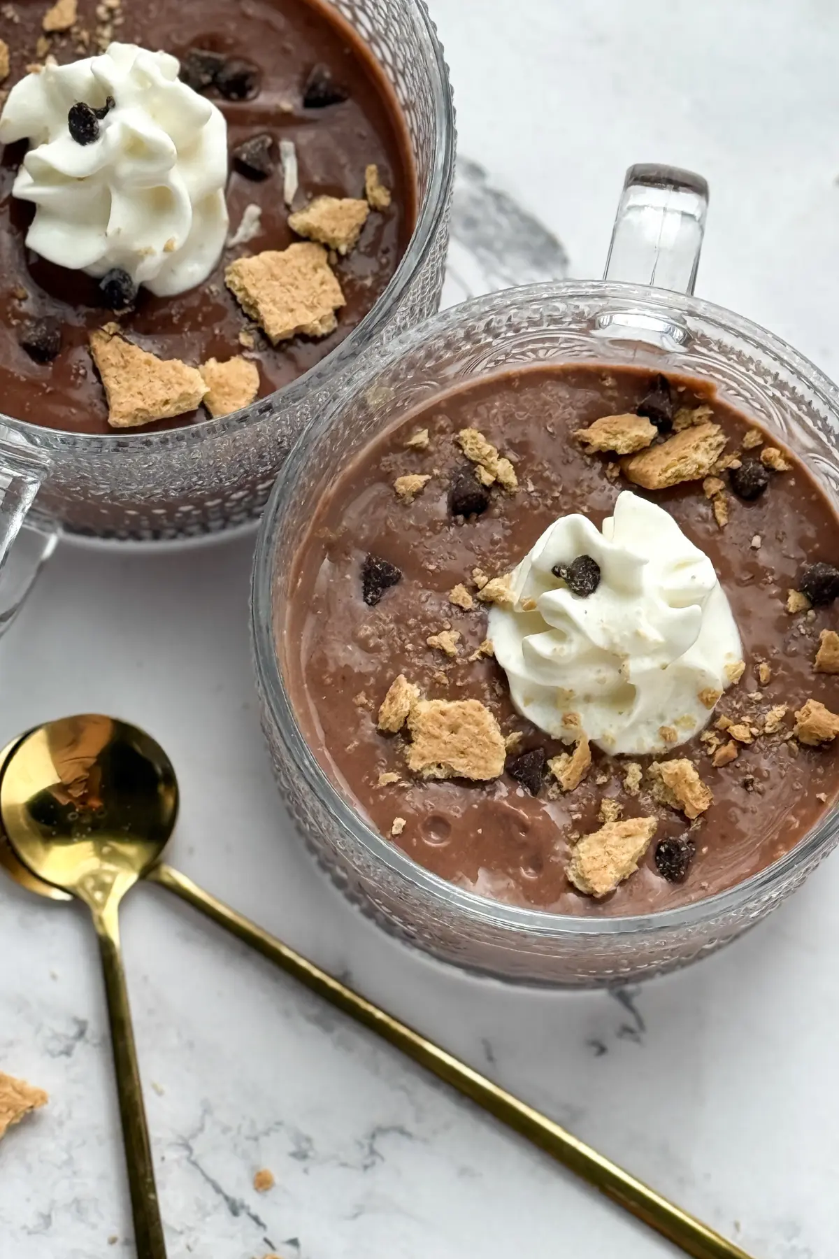 A birds-eye view of two dark chocolate puddings topped with whipped cream and graham crackers in bowls on a counter.