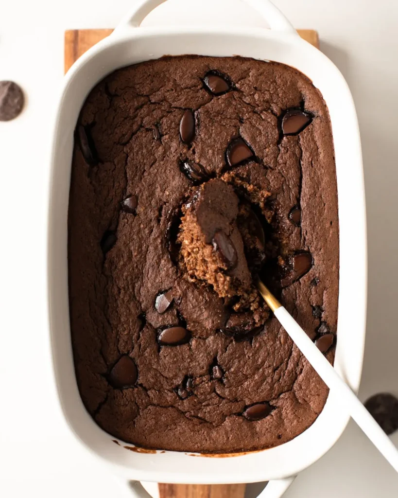 High protein chocolate baked oatmeal in a baking dish with a knife cutting through it.