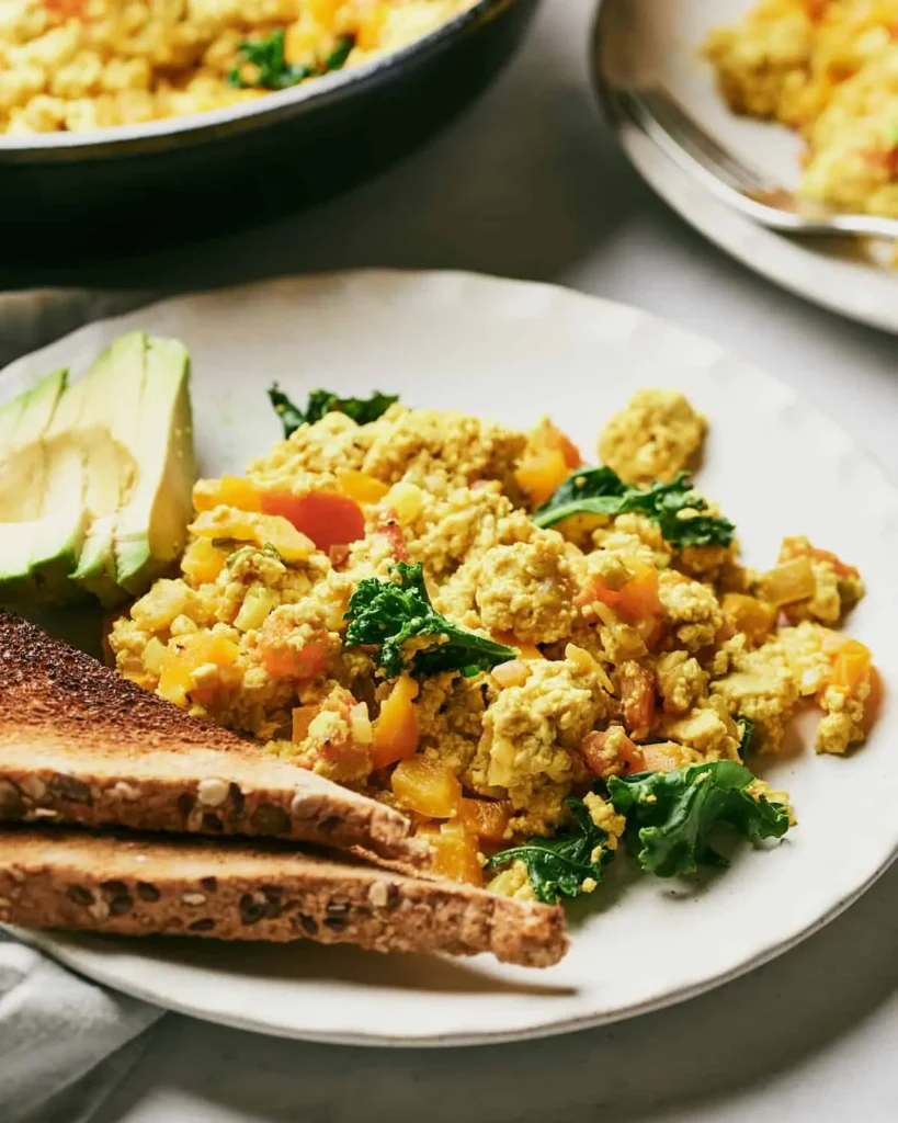 A gluten-free and dairy-free tofu scramble on a plate with sliced toast and avocado.