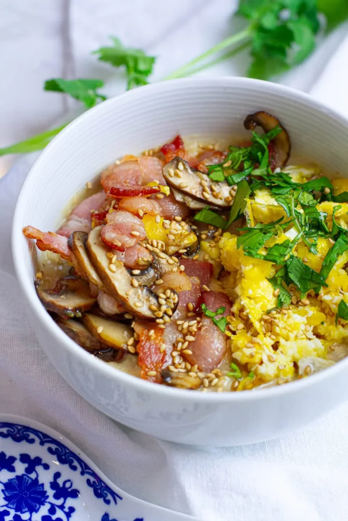 A savory bowl of oatmeal topped with bacon and scrambled eggs on a table.