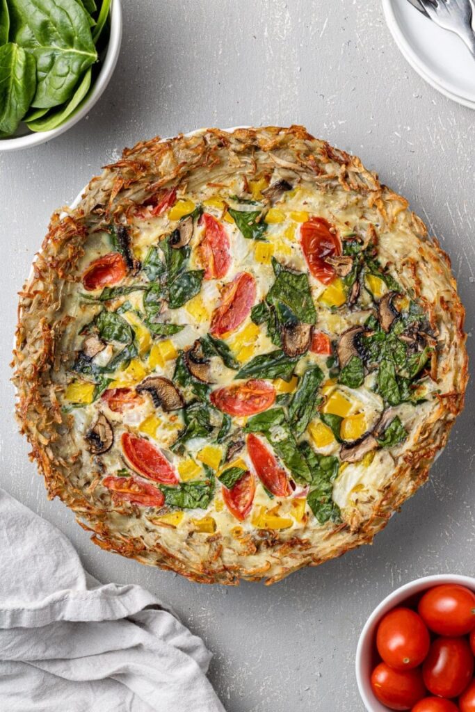 A gluten-free, dairy-free quiche with a potato crust and fresh spinach on a counter.