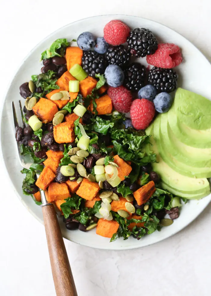 Black bean, sweet potatoes, berries and sliced avocado on a plate with a fork.