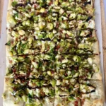 Brussel sprout, goat cheese and pancetta pizza on a baking sheet drizzled with balsamic glaze.