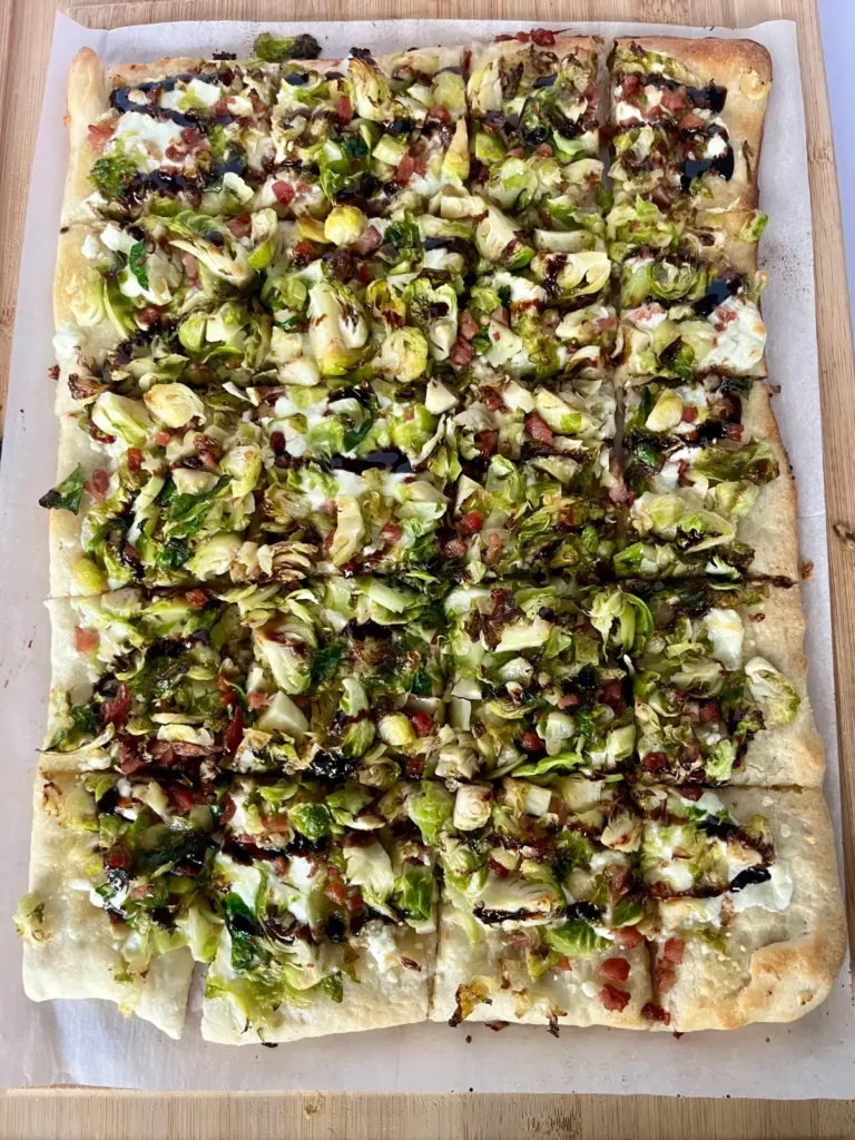 Brussel sprout, goat cheese and pancetta pizza on a baking sheet drizzled with balsamic glaze.