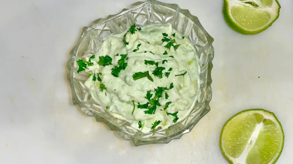 Greek yogurt avocado cream sauce in a glass bowl on a cutting board next to a lime cut in half.