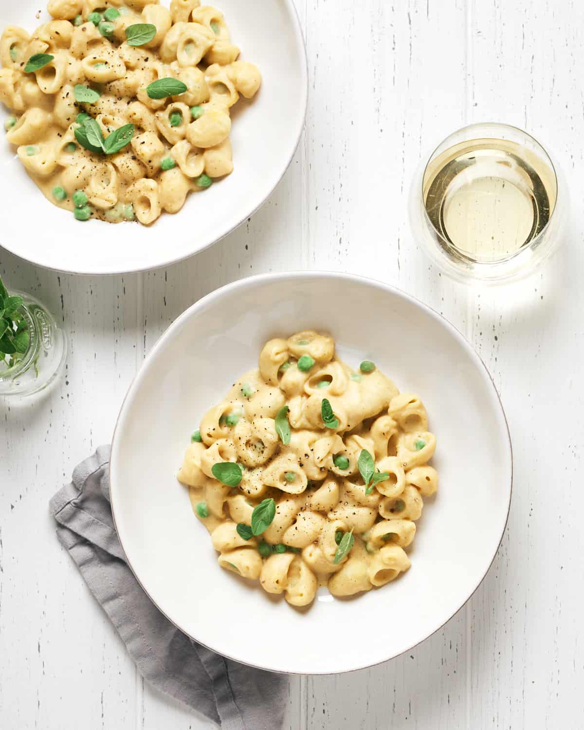 Two bowls of pasta with peas on a white table. 