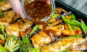 Chicken, broccoli, snow peas, and carrots on a sheet pan being drizzle with a honey garlic sauce for a lazy Sunday dinner idea.