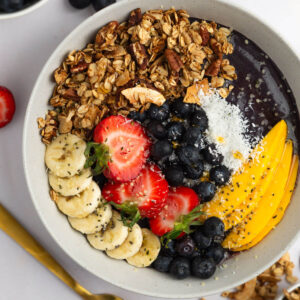 A protein acai bowl topped with lots of fresh fruits like bananas, strawberries and chopped nuts.