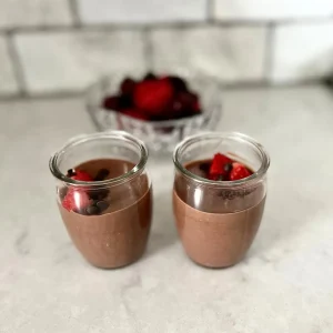 Two mini dark chocolate cheesecake cups topped with mini chocolate chips on a counter with a bowl of berries in the background.