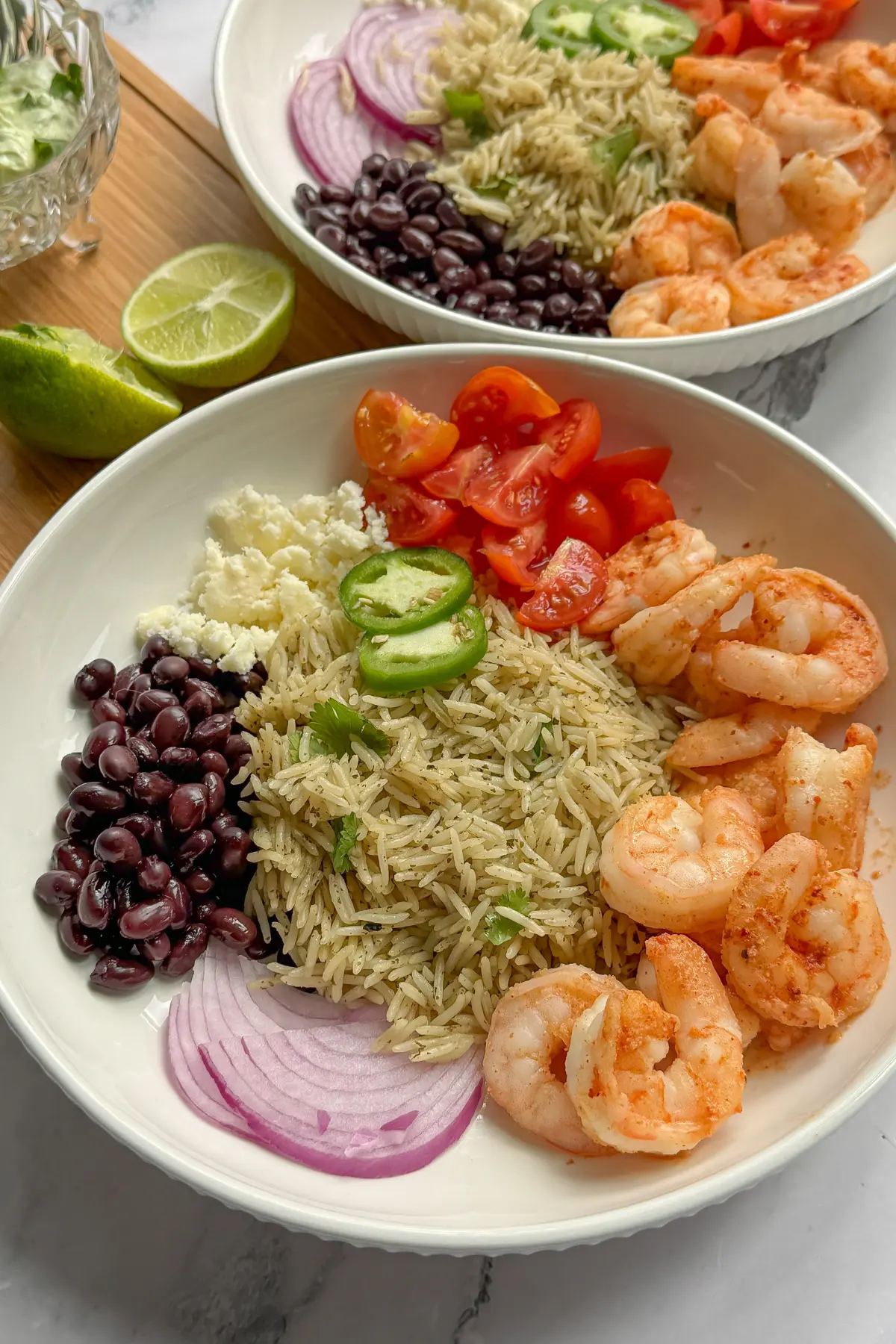 Two shrimp taco bowls next to a bowl of Greek yogurt avocado cream sauce on a counter.
