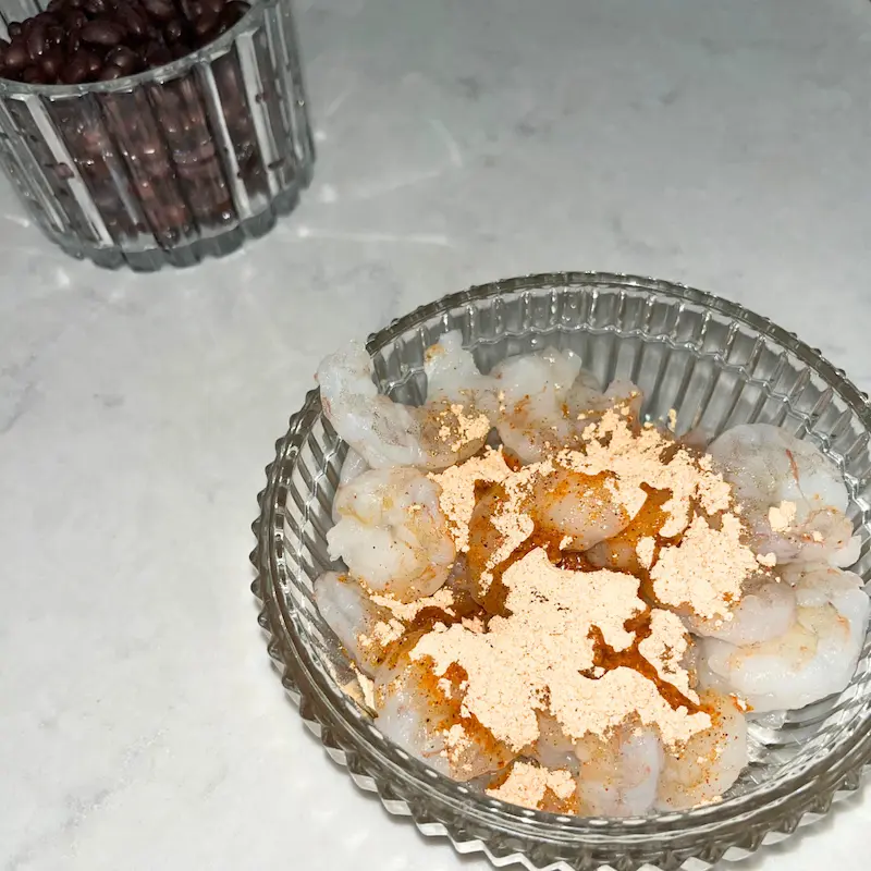 A bowl of raw shrimp with taco seasoning and olive oil.