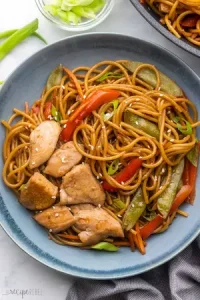 Teriyaki noodles, sliced chicken, and vegetables on a plate on the table for a lazy Sunday dinner idea.