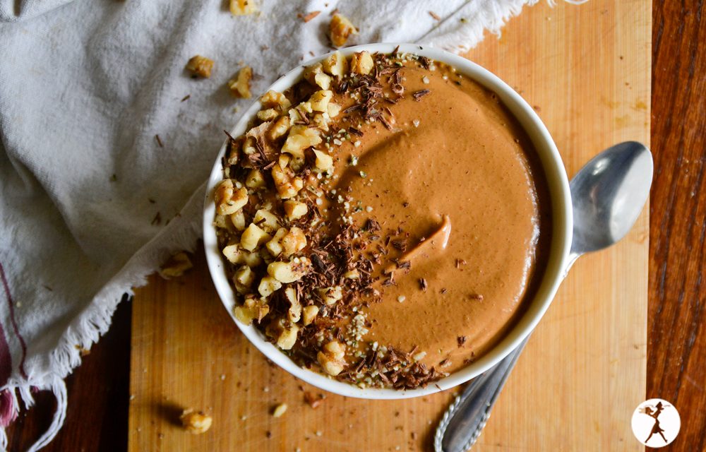 A sweet potato smoothie bowl on a wooden cutting board next to a spoon.