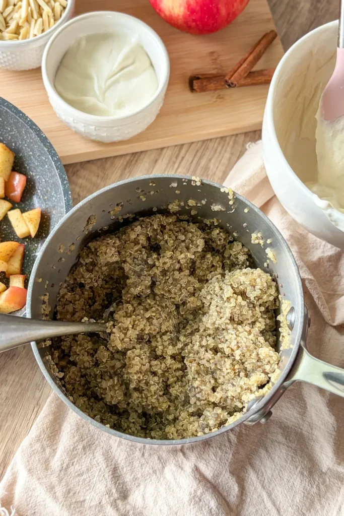 A birds-eye view of a pot of quinoa next to the cinnamon apples and a bowl of the cheesecake yogurt on a table.
