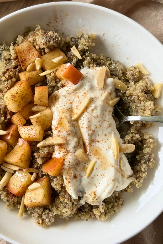 A close-up of a quinoa breakfast bowl topped with apples, Greek yogurt cheesecake frosting, and slivered almonds in a bowl.