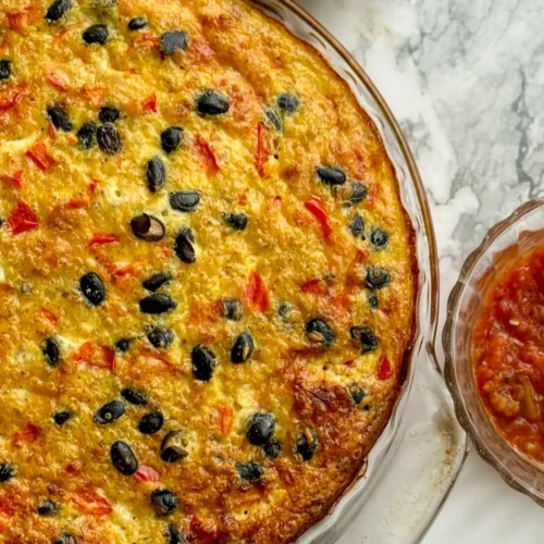 A birds-eye view of a baked quinoa and egg casserole on a counter next to salsa and an avocado.