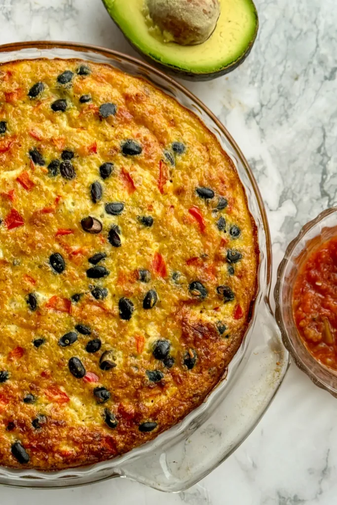 A birds-eye view of a baked quinoa and egg casserole on a counter next to salsa and an avocado.