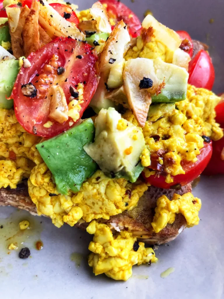 A close-up of a tofu bowl with diced tomatoes and avocado.