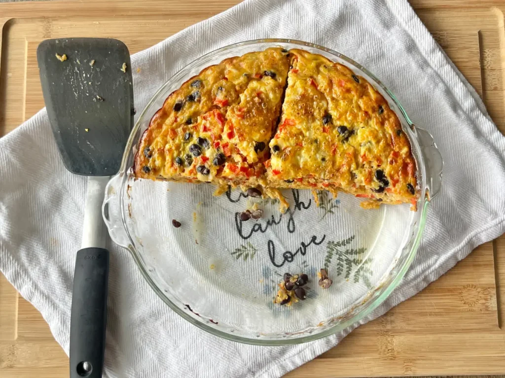 Two slices of quinoa breakfast bake in a glass baking dish on a cutting board next to a spatula.