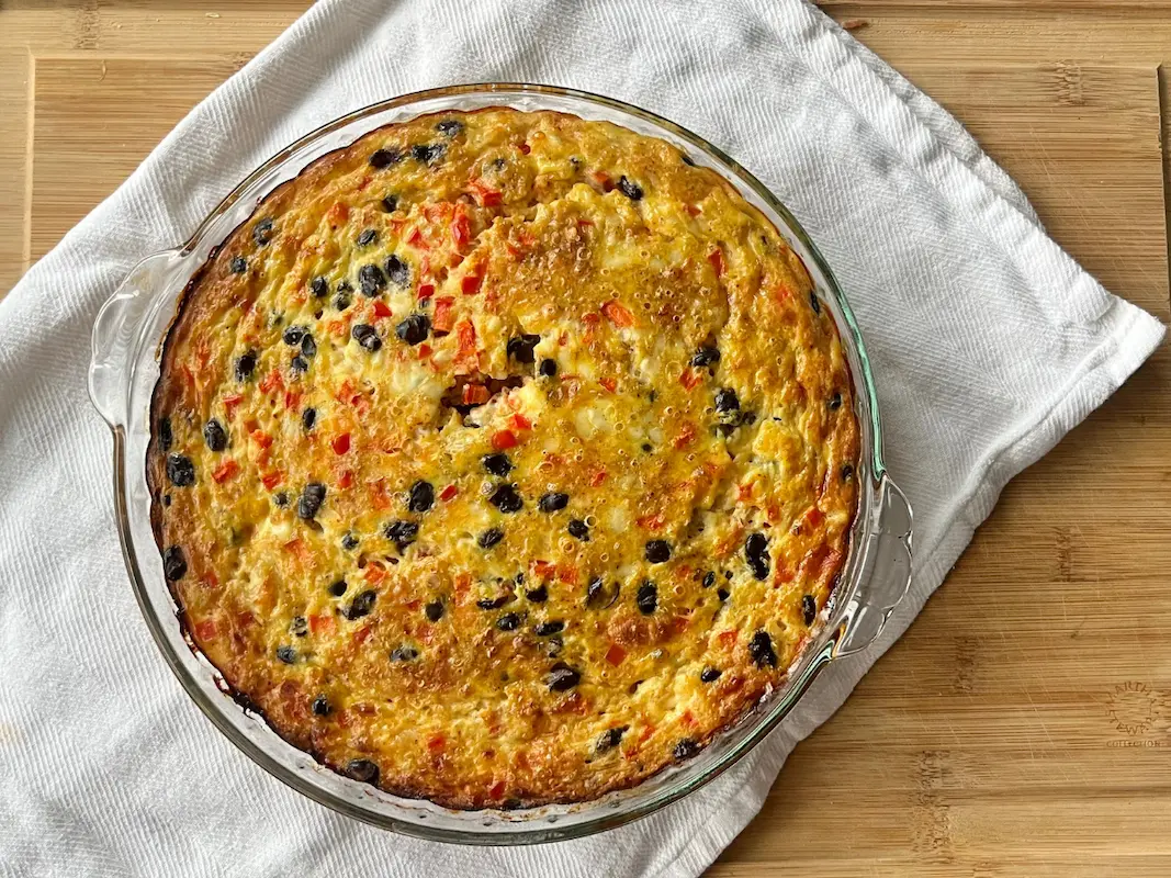 A savory quinoa breakfast bake in a baking dish on a white towel on a cutting board.