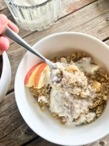 A bowl of quinoa with chia seeds topped with apple slices with a Greek yogurt and maple syrup mixture on a wooden board.