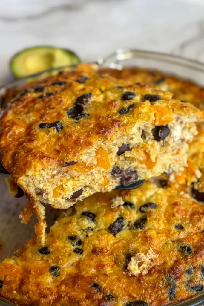 A close-up of the side of a slice of quinoa bake on a spatula with the bake in the background.