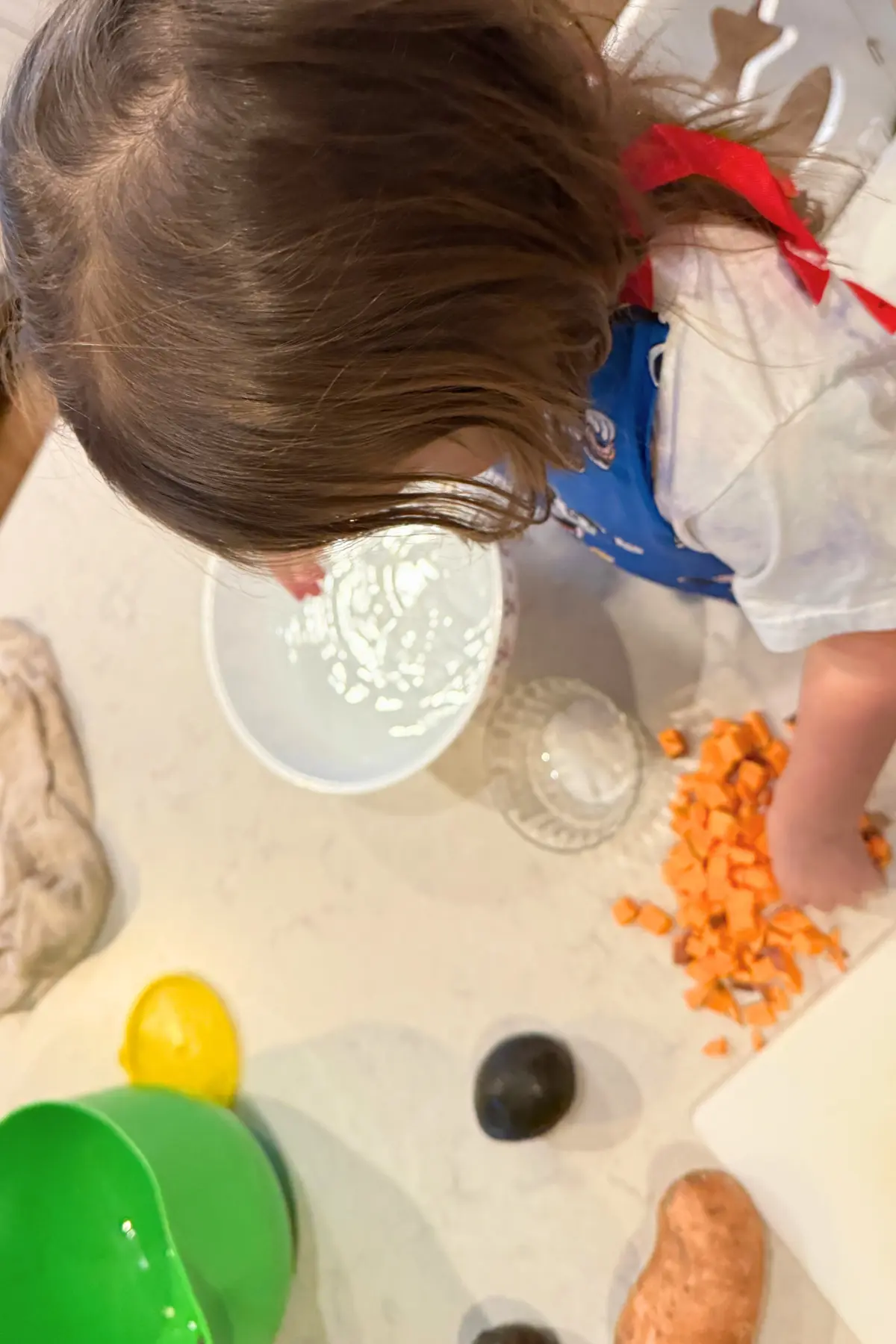 A toddler helping make dinner on a stool in the kitchen.
